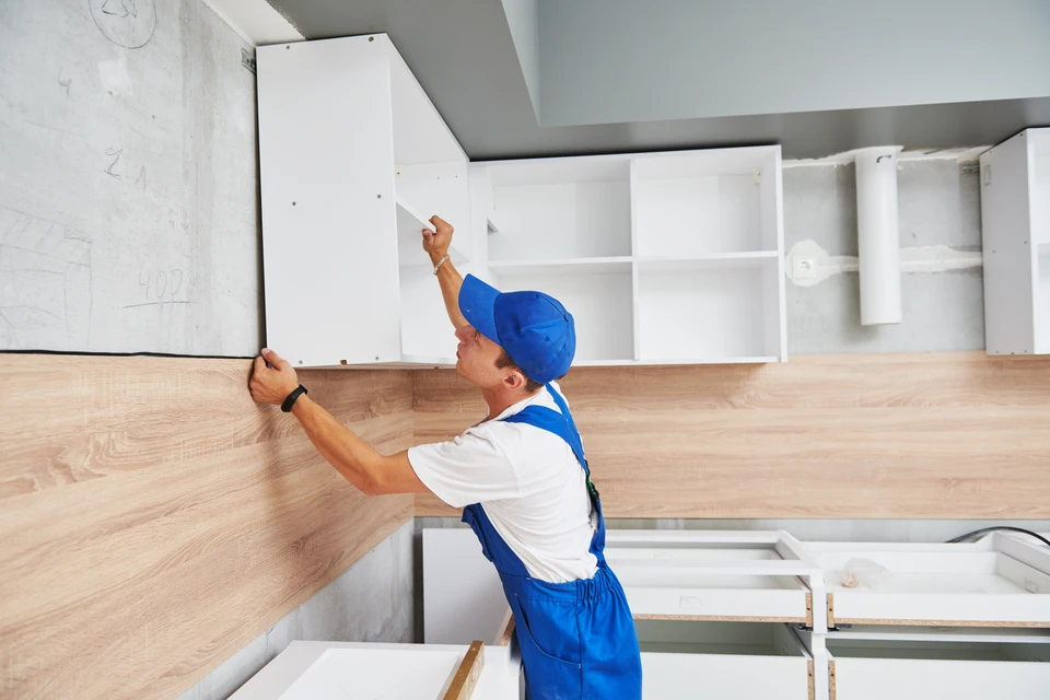 Ouvrier en salopette bleue et casquette installant une cuisine équipée moderne