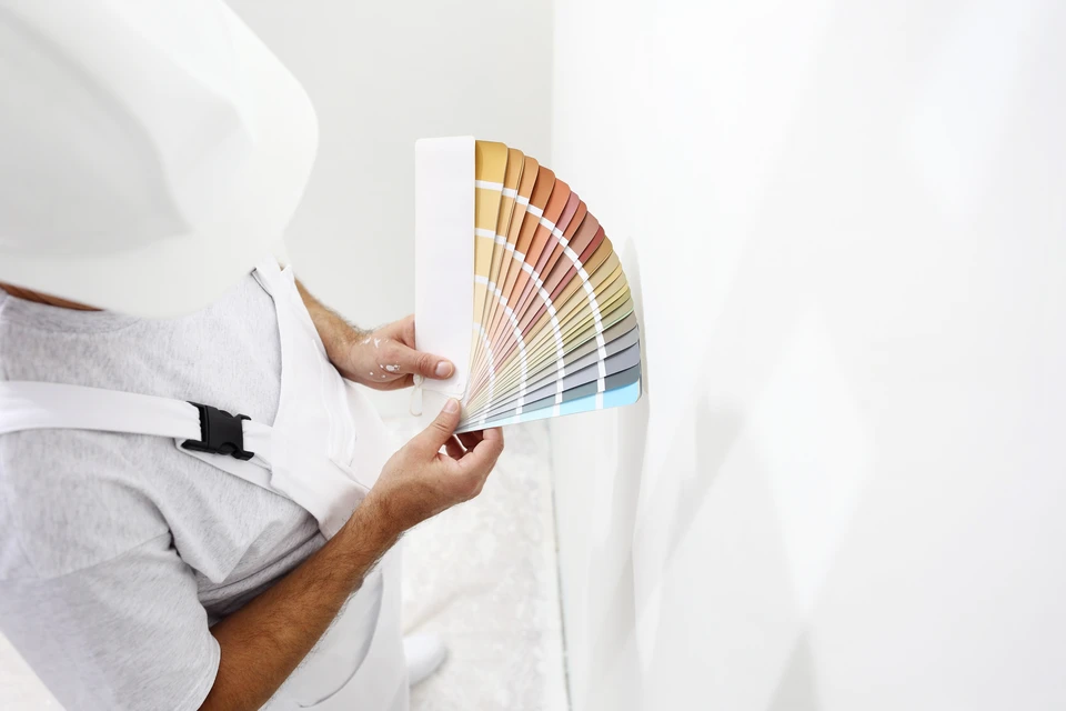Homme en veste grise tenant un nuancier de couleurs déployé en éventail dans un intérieur blanc épuré