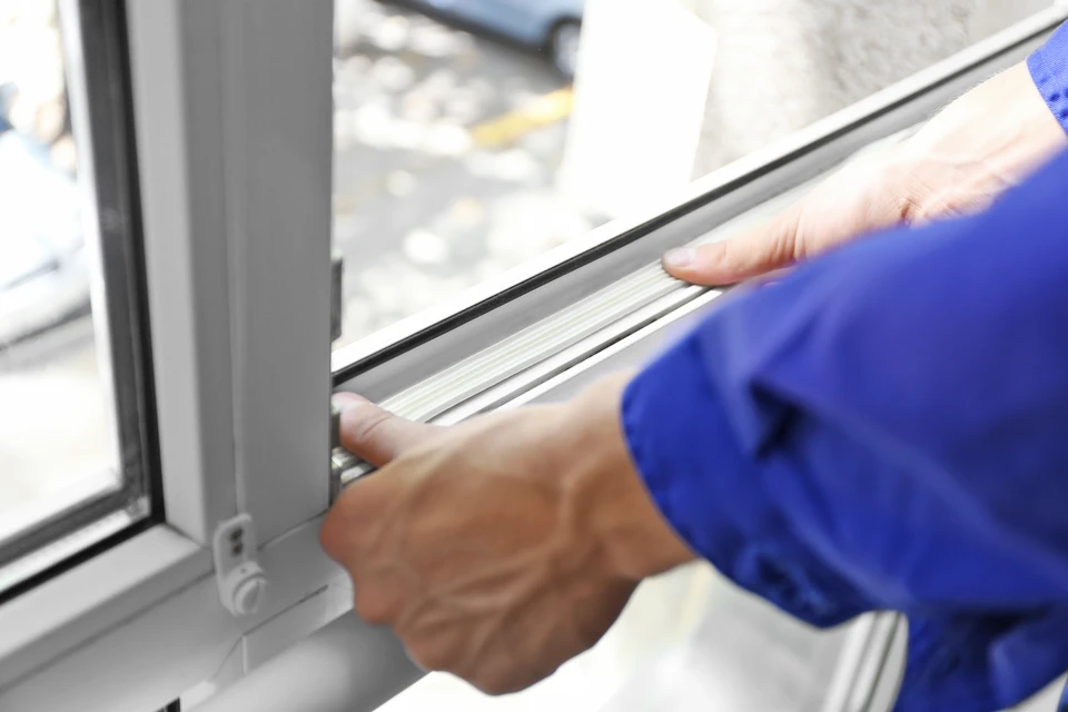 Artisan en vêtement de travail bleu effectuant la pose d'un joint d'étanchéité sur une fenêtre PVC blanc à double vitrage