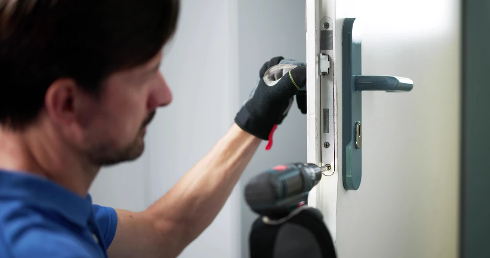 Ouvrier en tenue bleue et casquette installant une porte en bois dans un intérieur résidentiel en construction